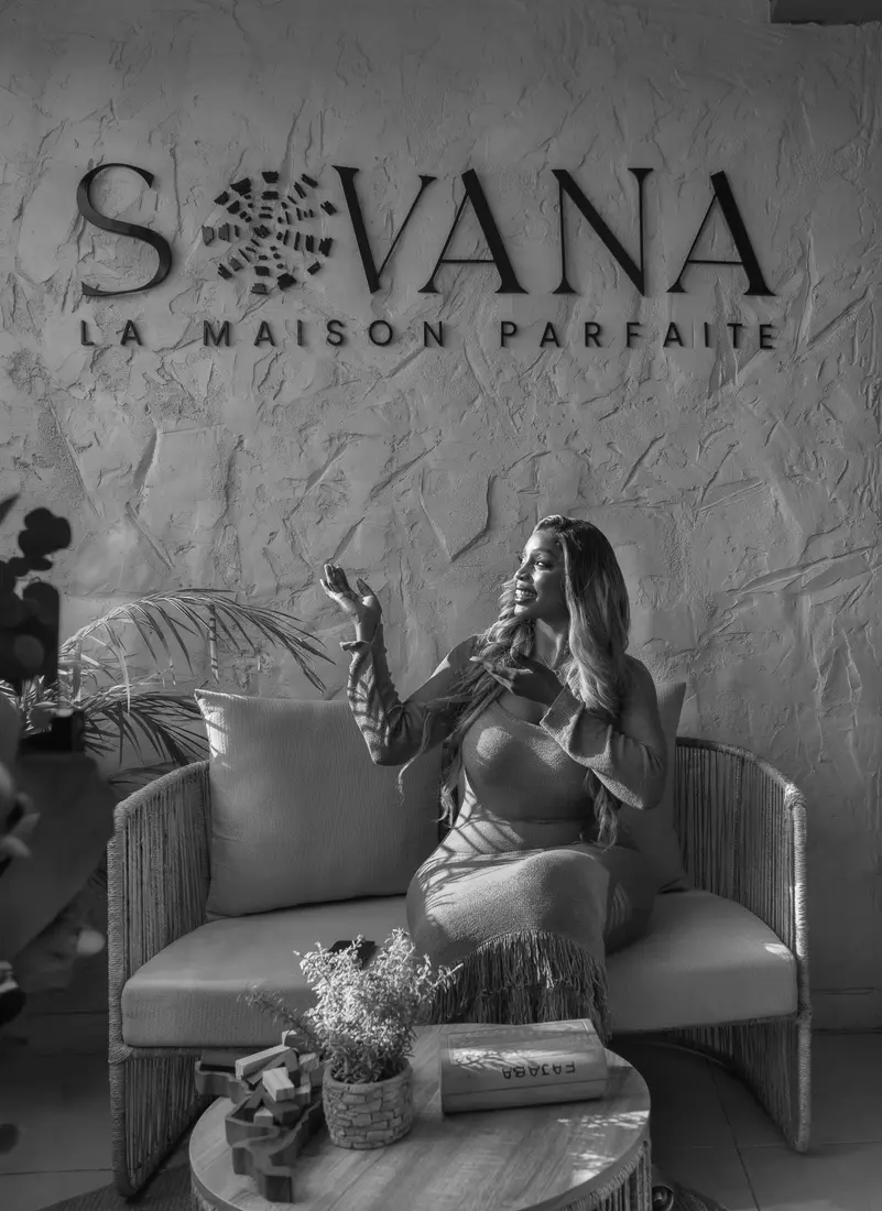 Portrait en noir et blanc de la fondatrice, assise dans un fauteuil devant le mur logo